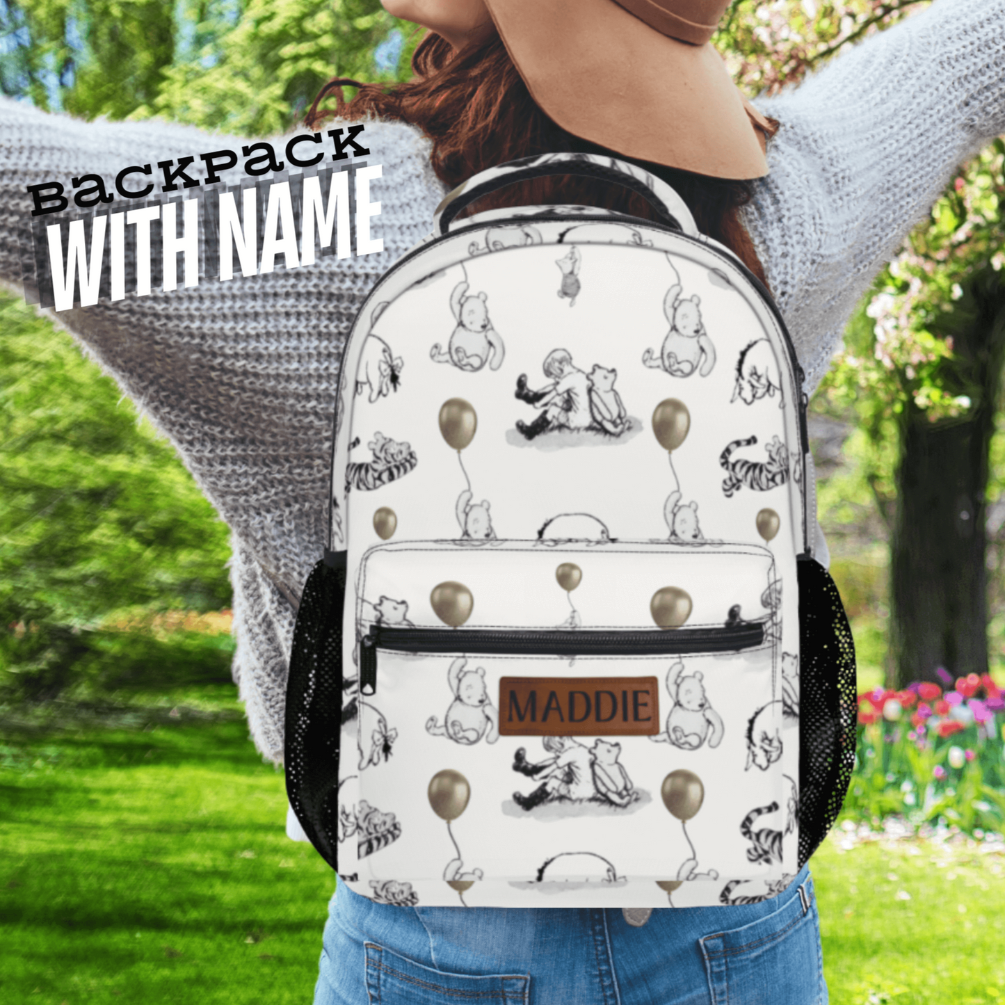 Person wearing a white backpack with black illustrations in an outdoor setting with a winnie the pooh and characters on the backpack and its personalized with name