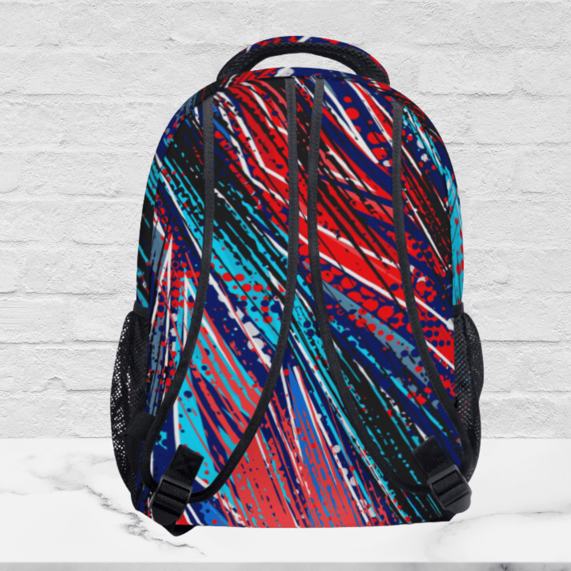 The backside of our backpack shows the same paint splatter pattern all over the padded shoulder straps and black adjusting buckles.