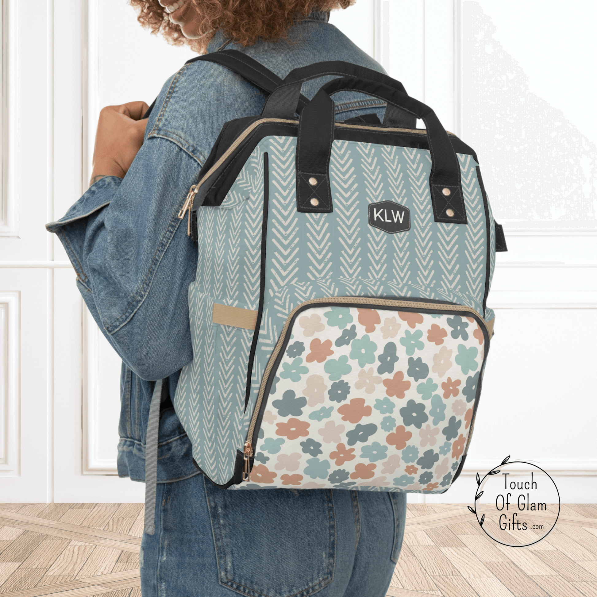 Our Boho Diaper bag backpack has a sage green fabric with distressed arrows and the front outer zippered pocket has colorful boho flowers. This diaper bag is shown as a diaper backpack with the black monogrammed patch.