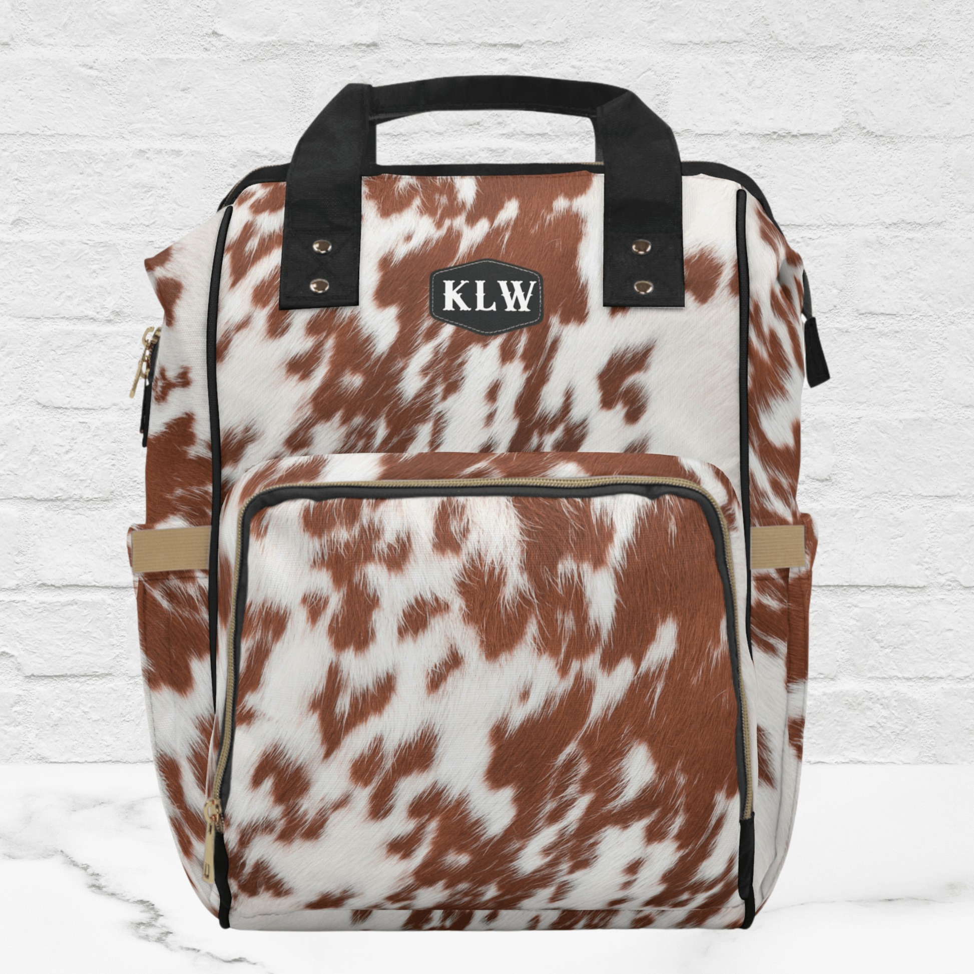 Our Western style cowhide print diaper bag backpack is rust and white cowhide with black handles and black patch for monogram