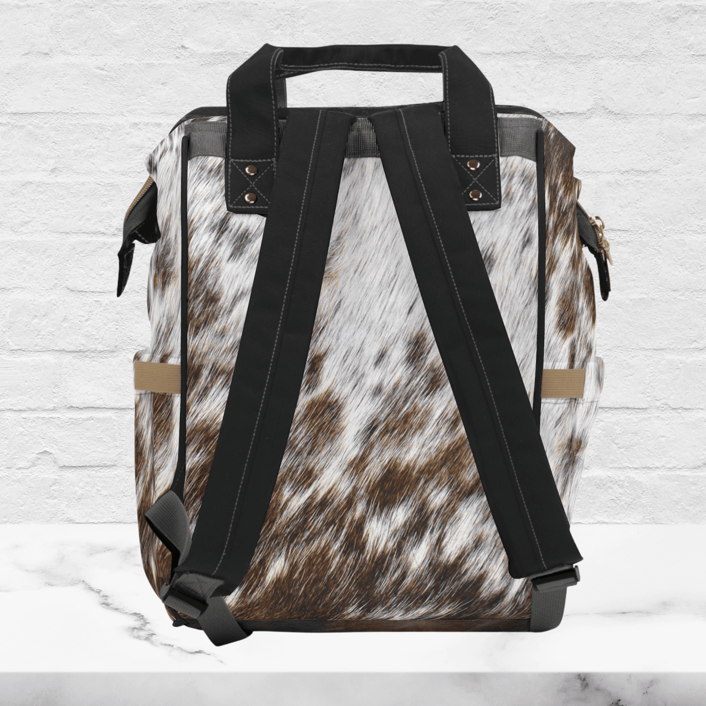 The back of our multipurpose airport backpack for women shows the beautiful cowhide print with black padded adjustable straps and black piping around the edges .