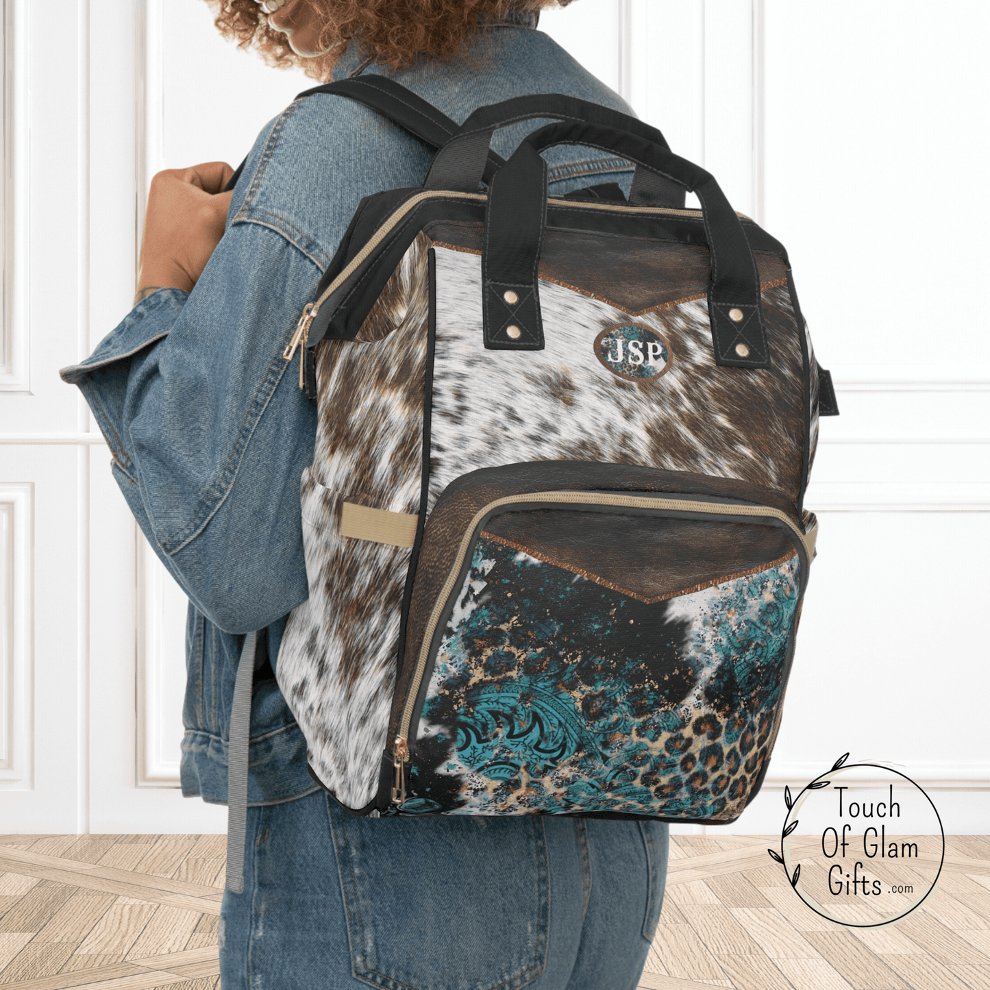 This custom diaper bag backpack is a cowhide print with brown leather print on durable nylon fabric. The front exterior zippered compartment has a print with cowhide, leopard print and turquoise for a western look on this multipurpose diaper backpack.