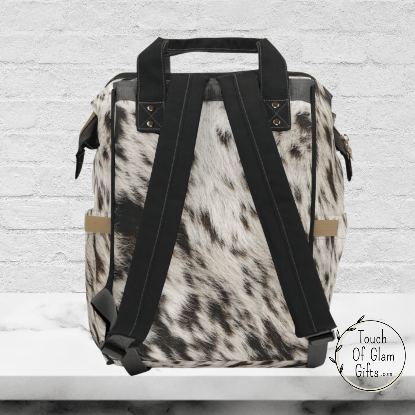 The back side of our cow print backpack shows black padded shoulder straps and a black carrying handle.