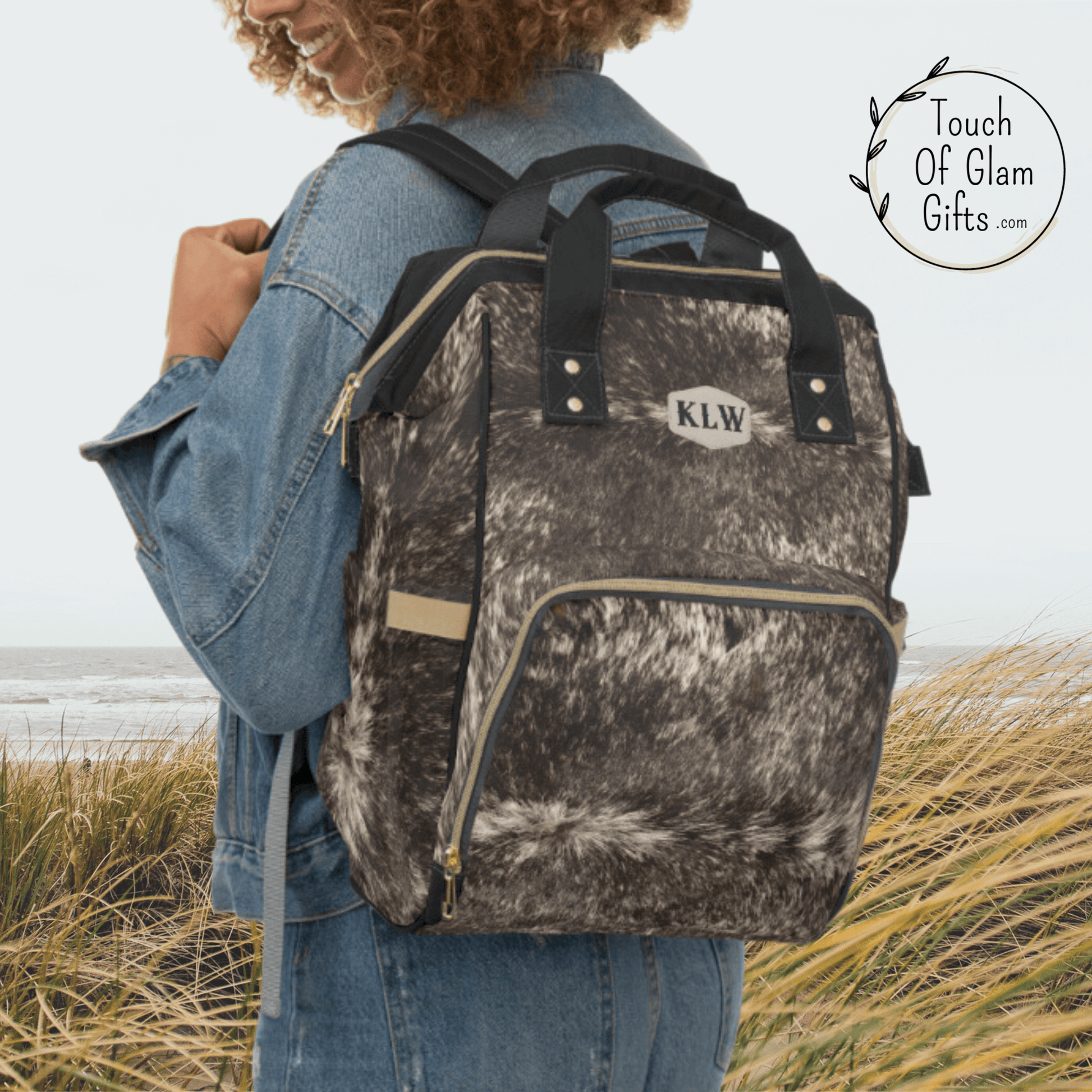 Our brown cowhide backpack is shown on a female cowgirl wearing the padded shoulder straps over her shoulders. THe backpack has monogramming in a western style.