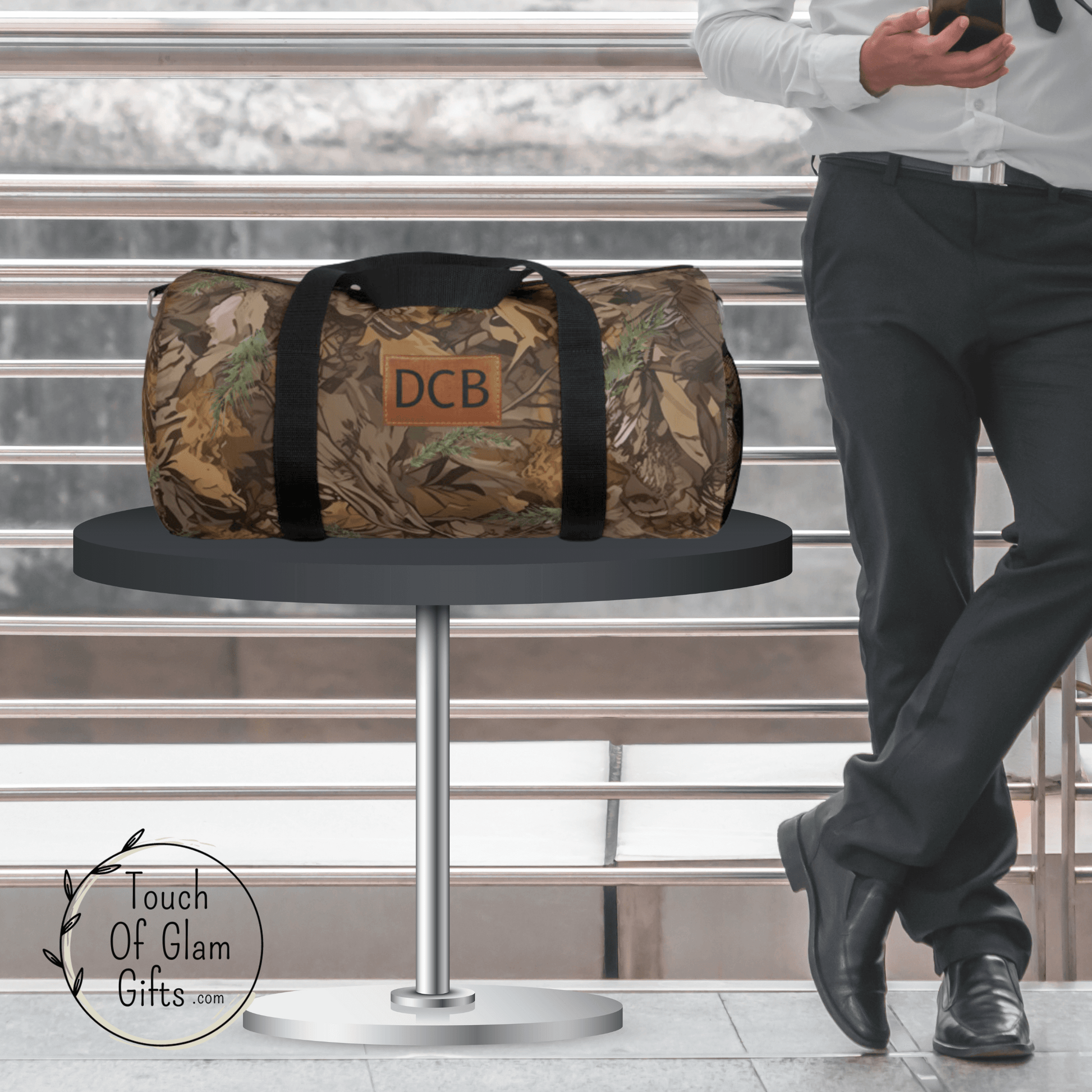 A business man standing next to a table with the large camouflage duffel bag with shoulder strap and his monogrammed initials on the bag.