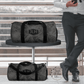 The perfect personalized travel gear for business men. This shows a man checking his phone at the airport with the large monogrammed duffel bag on a table and the small carry on duffel on the floor.