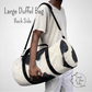 Our large black and white cow print duffel bag is shown over the shoulder on a male model to show the size of the large bag and the metal hardware on the shoulder strap.