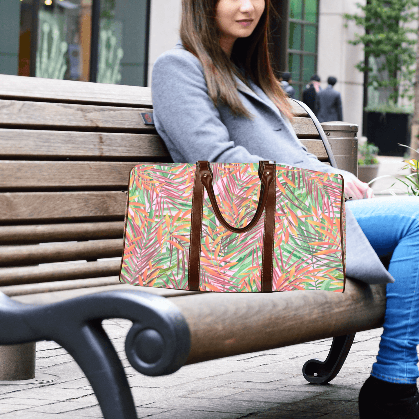 This stylish flight bag in our tropical leaf color scheme looks great with whatever your outfit is. This woman is sitting on a bench.