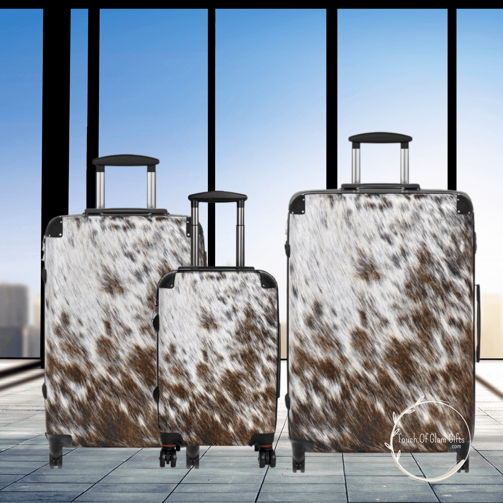 Our beautiful 3 piece cowhide luggage set shown in an airport with a glass window and blue sky background. The luggage pieces have 360 rotating wheels.